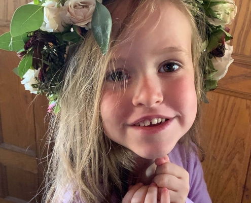 little girl smiles into camera with big flower crown on head